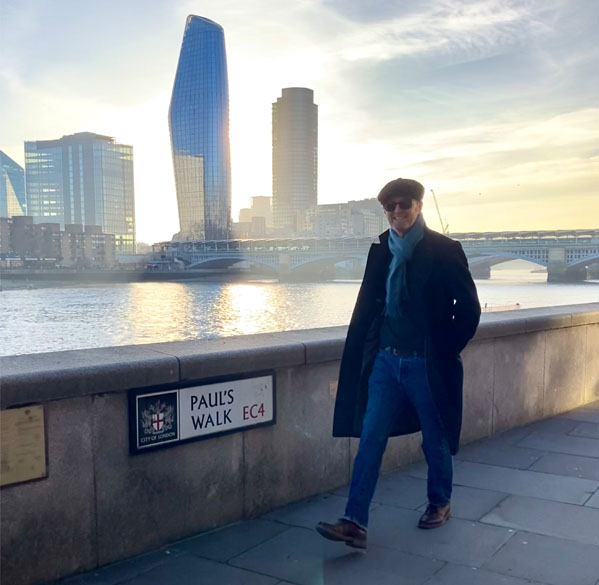 Photograph of illustrator, Paul Bateman walking along Paul's Walk by the River Thames with London skyline.